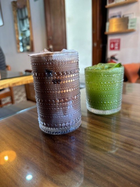 An iced coffee and a green matcha in textured glasses on a wooden table at ATTA Salón Café in Puebla