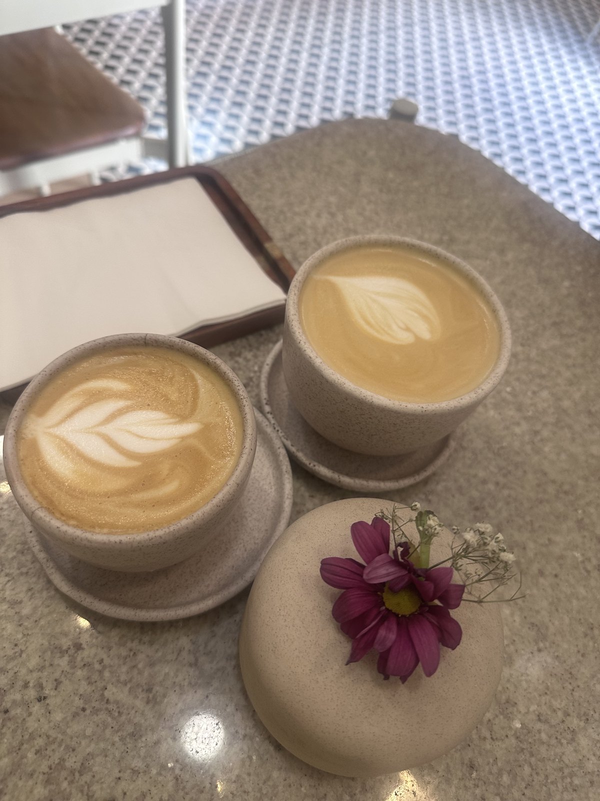 Two lattes with rosetta art on a stone table next to a purple flower at Calixto Café in Puebla