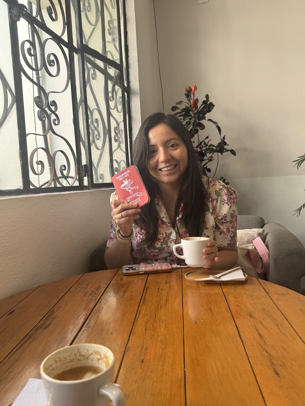 Diana holding the coffee passport at a wooden table by the window at Café Carmín in Cholula