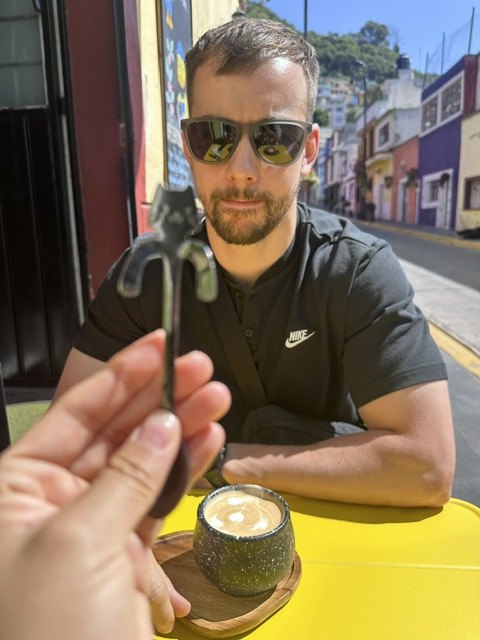 Zack at a yellow sidewalk table on a colourful street outside Cuac Café in Atlixco